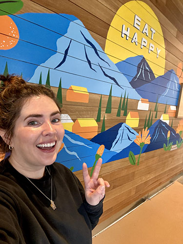 artist with mural she created in a restaurant